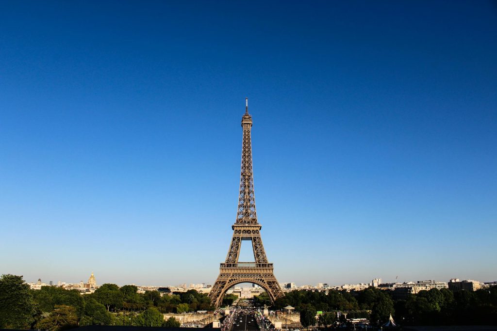 Eiffel Tower in Paris rising against a clear blue sky with trees and city below at the base