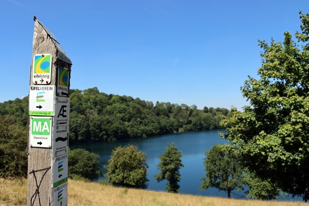 Eifelsteig Trail sign overlooking a scenic lake and forested hills for Hiking in Germany
