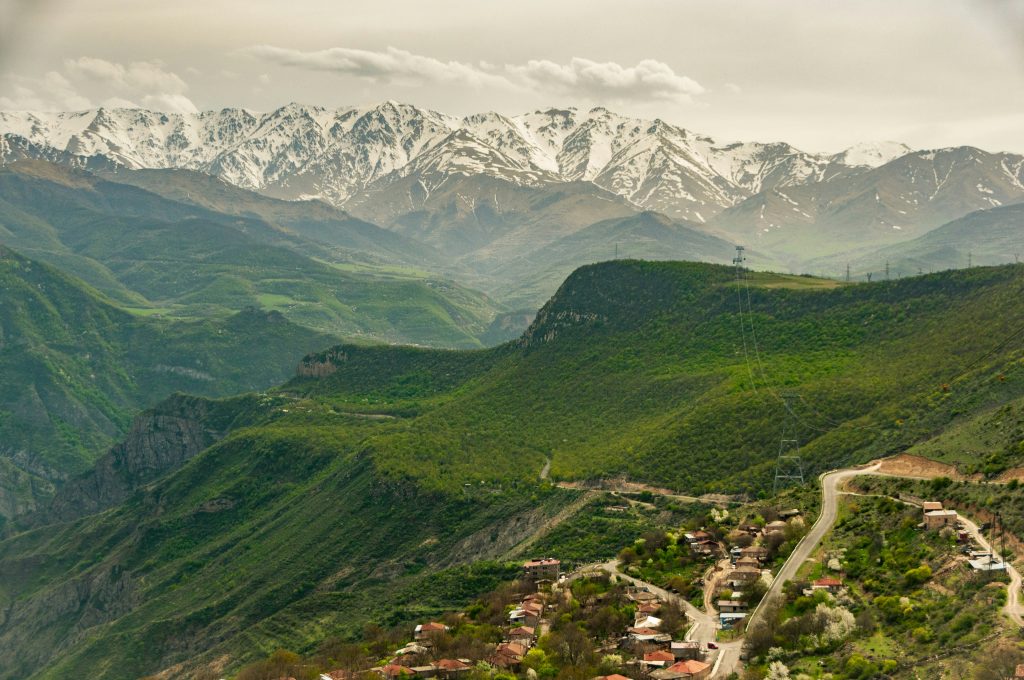 Scenic view of Armenia’s lush green hills leading up to snow-capped mountains, with a village nestled in the valley.