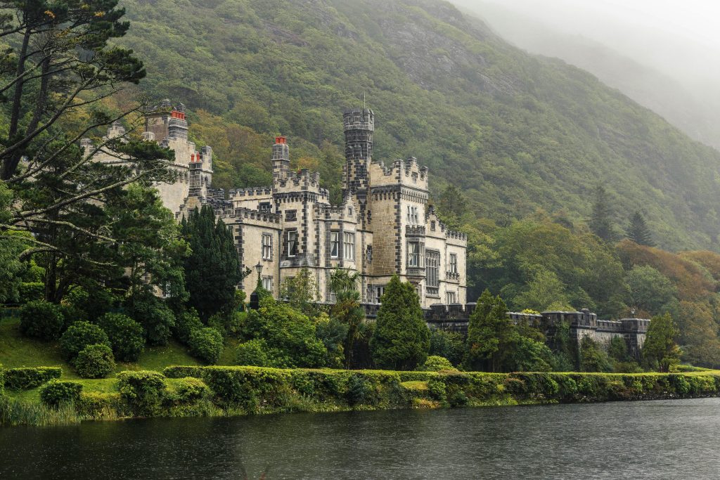 Kylemore Abbey in Connemara, Ireland, a Gothic-style castle with towered turrets, surrounded by lush greenery and a reflective lake. Perfect for hiking in Ireland.