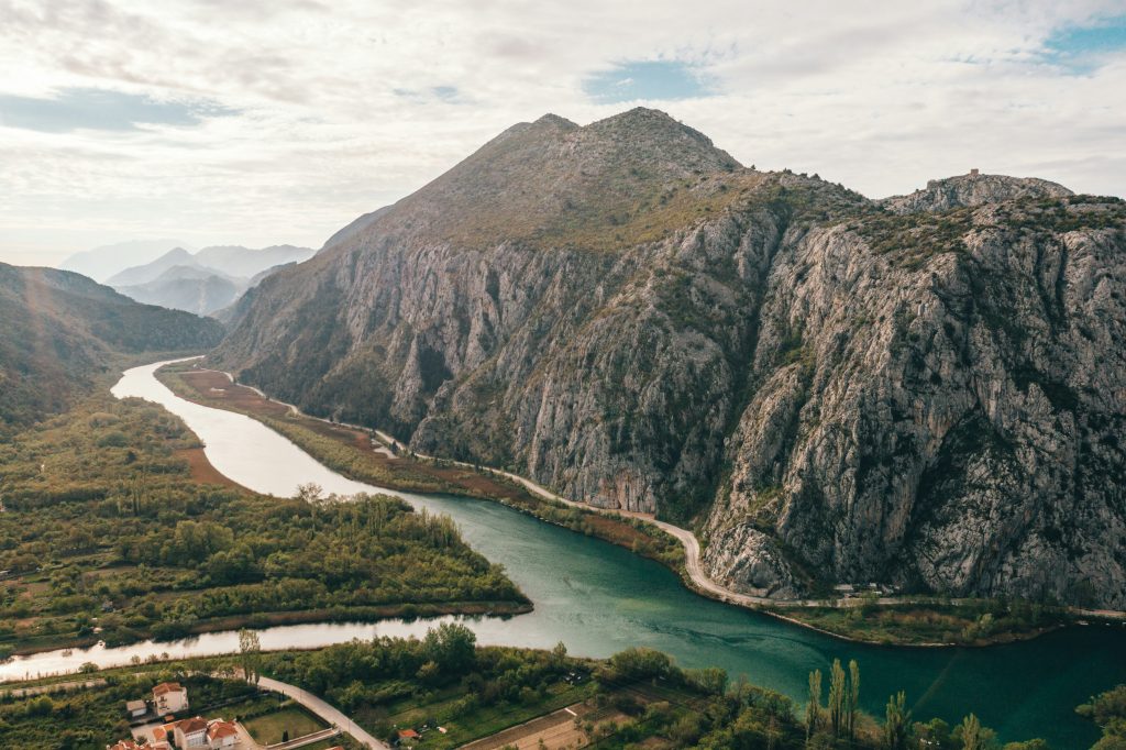 Stunning aerial view of Croatia’s rugged mountains, winding river, and lush greenery, offering a serene natural landscape.