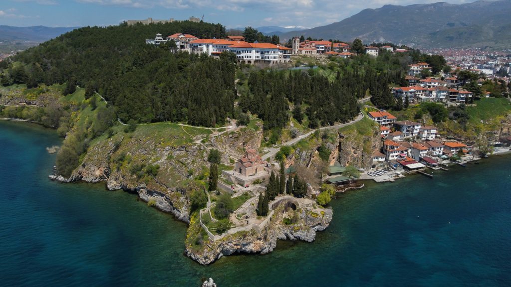 Aerial view of Ohrid, North Macedonia, showcasing hills, historic buildings, and lakeside homes along crystal-clear waters.