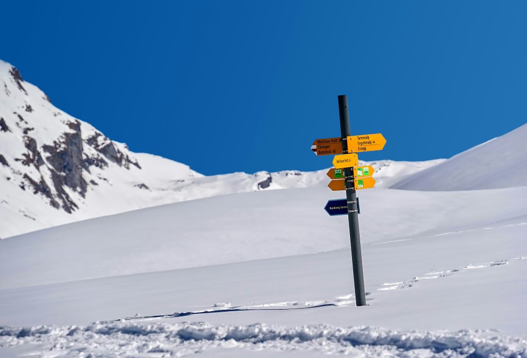 Directional signposts in a snowy mountain landscape, marking various hiking routes for point-to-point walking in the winter.