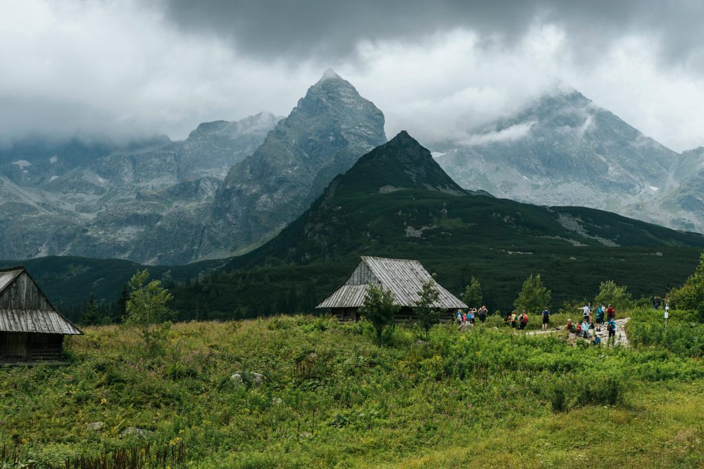 Hikers exploring Poland's Carpathian and Tatra mountains, with rustic cabins and towering peaks under cloudy skies.