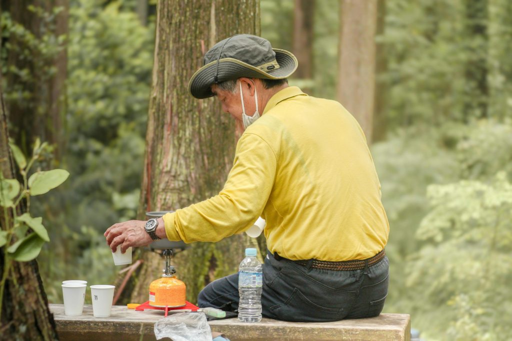 Senior man making a drink in the forest with a portable stove, highlighting a relaxing moment during a senior hiking adventure.