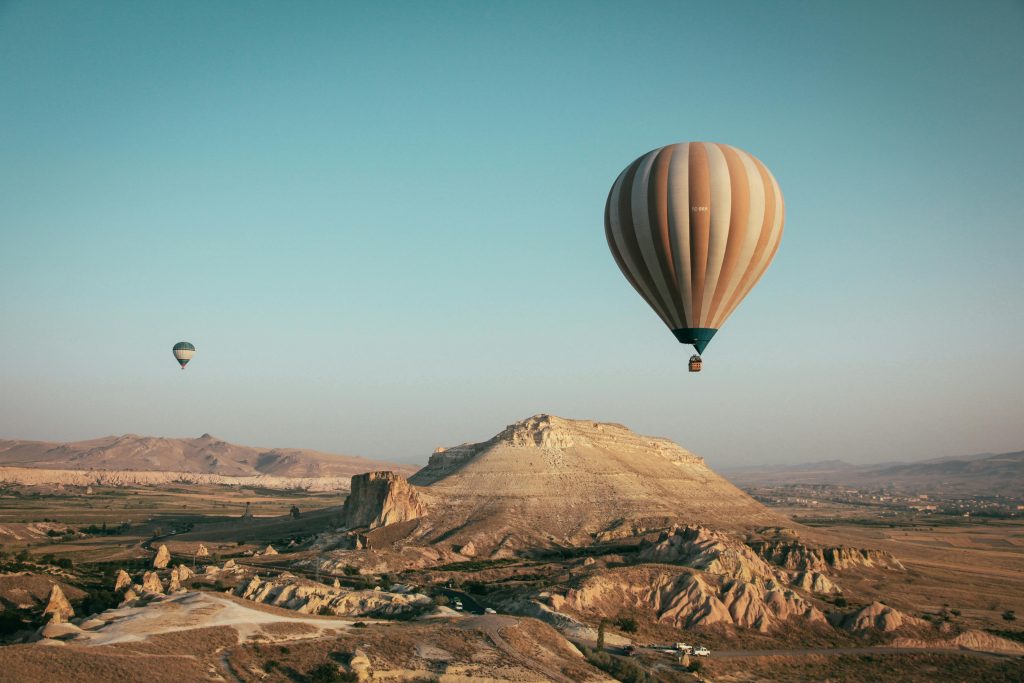 Hot air balloons flying over Cappadocia, Turkey, with unique rock formations and a vast desert landscape below.