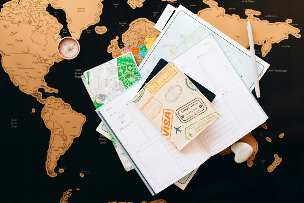 Passport with visa stamps, travel maps, and a planner on a world map, indicating visa requirements and travel planning.