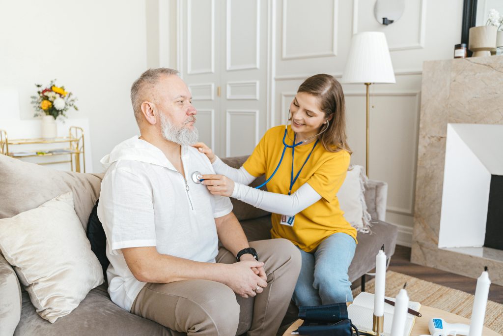 Nurse performing a health check on an elderly man with a stethoscope, ensuring senior safety and well-being at home.