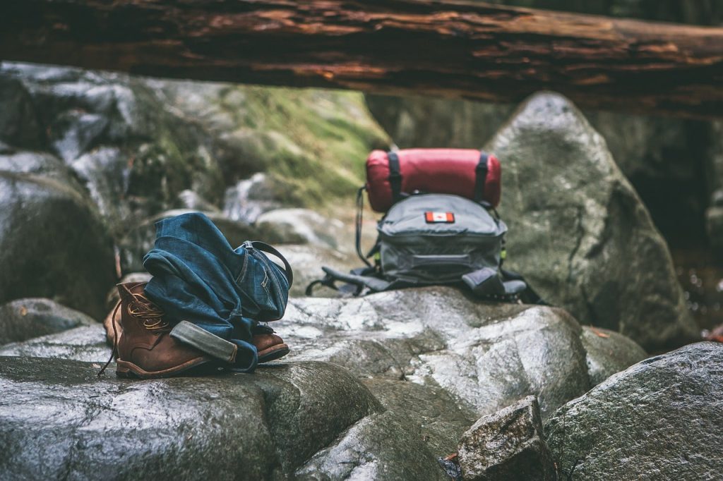 A hiking backpack, boots, and jeans rest on wet rocks in a forested area, evoking an outdoor adventure and the best hikes in Denmark.
