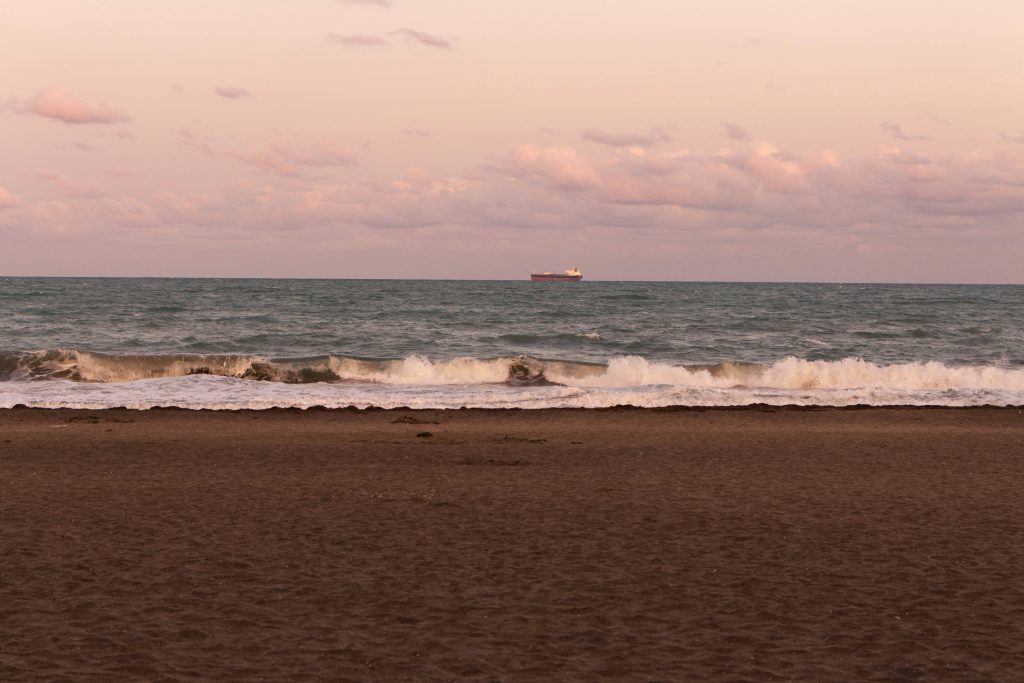 Calm beach with rolling waves and a distant ship on the horizon, showcasing a serene coastal landscape perfect for hiking tours in Bulgaria.