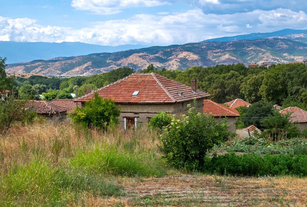 Scenic view of traditional houses with red roofs in Bulgaria, nestled among green fields and rolling mountains, ideal for an Eastern Balkan hiking adventure.