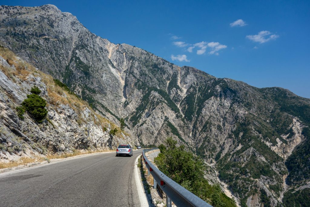 A car drives along the winding road through Llogara Pass, offering breathtaking views of the rugged mountains, part of Albania's popular hiking trails.
