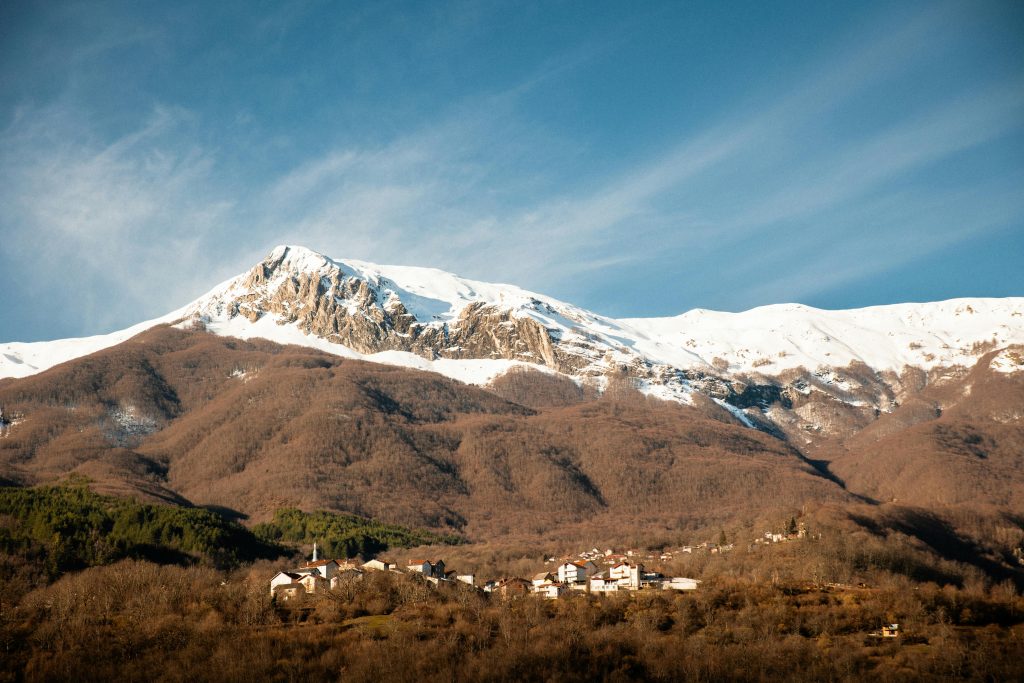 Snow-covered Mount Korab rises above a village, offering some of the best mountain hikes in Albania with breathtaking views and rugged terrain.