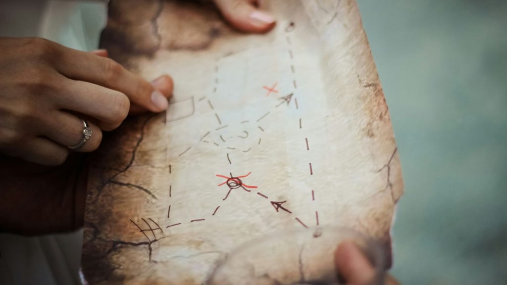 A person points to a hand-drawn map with red markings, indicating key locations for a scavenger hunt or outdoor recreation activity.