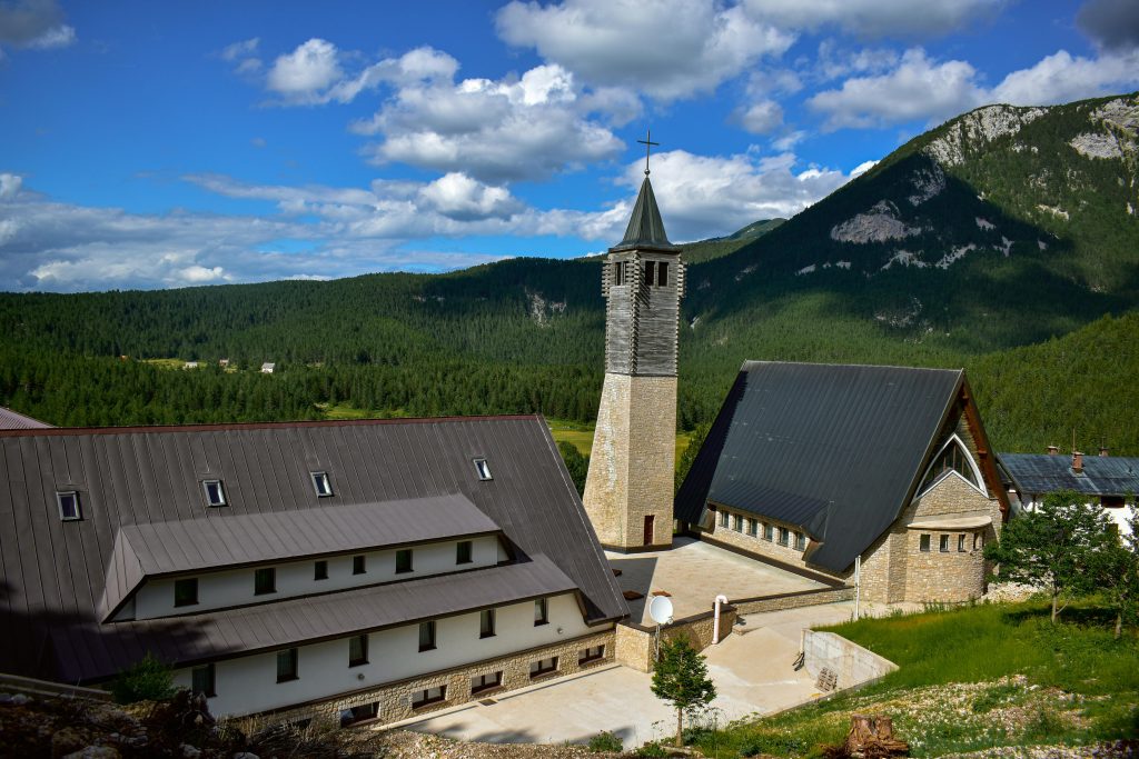 Scenic view of a church and surrounding mountains, offering picturesque hiking routes in Herzegovina amidst nature.