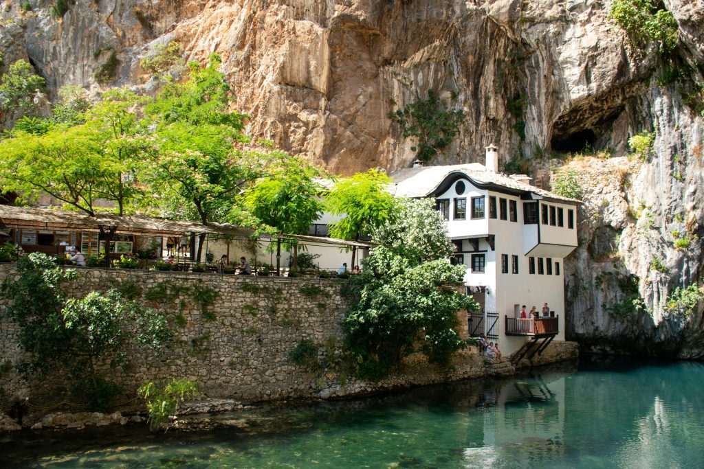 Traditional house by the river surrounded by lush greenery and cliffs, one of the best hiking spots in Bosnia and Herzegovina.
