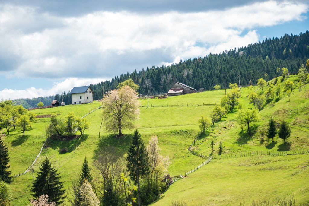 Serene countryside with green hills, a house, and forests, offering peaceful outdoor activities in Bosnia.