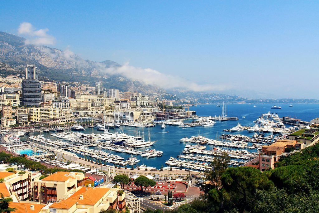 A breathtaking view of Monte Carlo's harbor with luxury yachts, modern buildings, and coastal mountains, ideal for hiking in Monte Carlo's scenic landscapes.