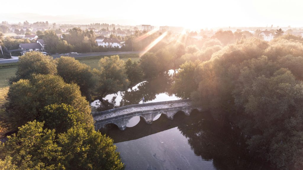 A scenic view of a stone bridge over a river surrounded by trees, perfect for nature walks in Herzegovina during sunset.