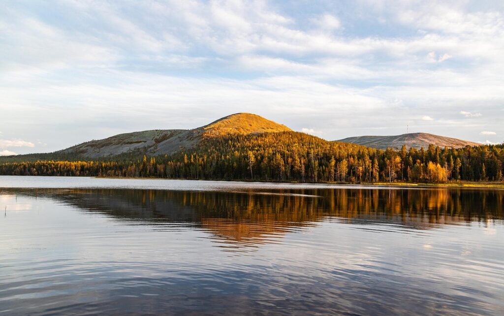 Golden autumn forest and mountain reflected in a calm lake, a scenic view along nature trails in Finland.