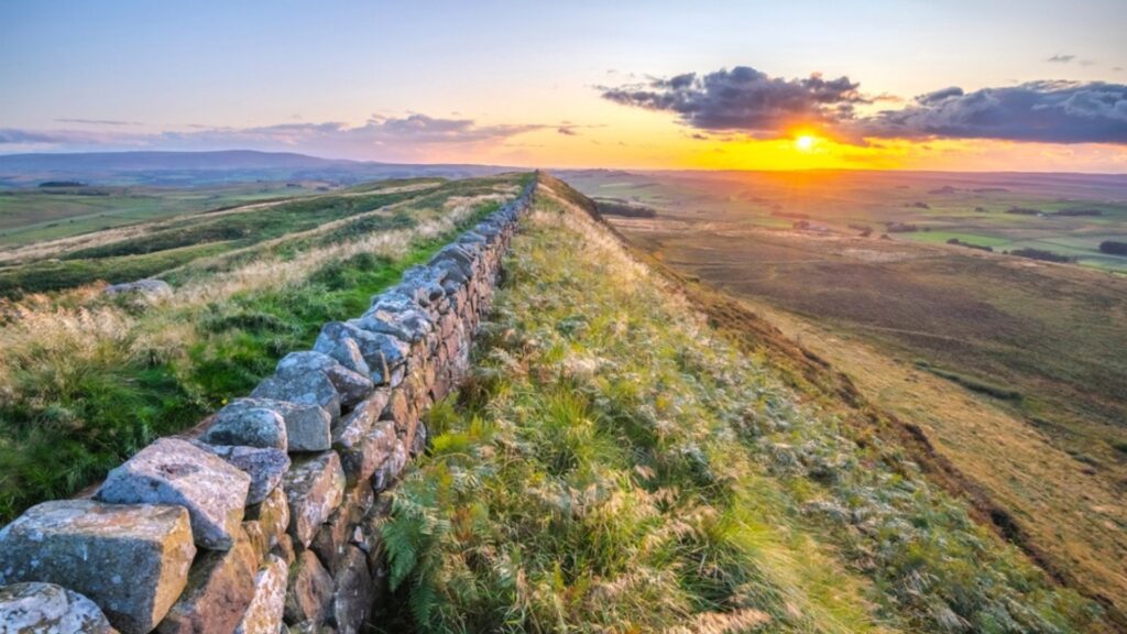 Scenic sunset view over Hadrian’s Wall in Northern England, featuring ancient stone ruins, rolling green hills, and golden light across the countryside — iconic British heritage landmark and popular walking route.