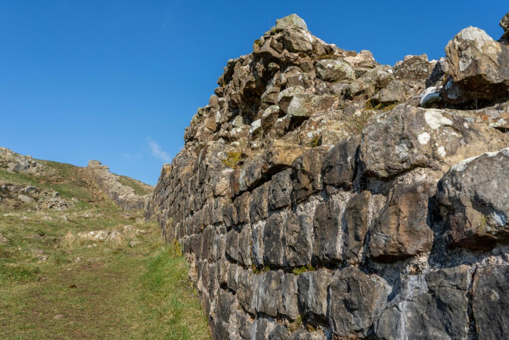 Close-up view of Hadrian’s Wall, a UNESCO World Heritage Site in Northern England, showing ancient Roman stonework under a bright blue sky and grassy landscape — historic British landmark.