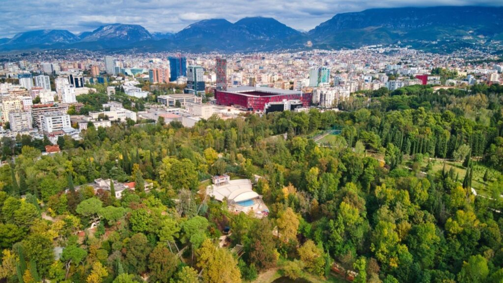 Aerial view of Tirana city skyline with lush Grand Park and surrounding mountains, perfect for a Tirana city travel guide.