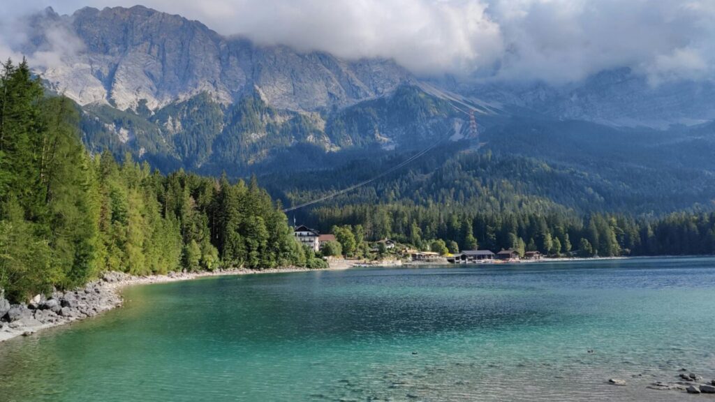 Clear turquoise lake in the Alps with forested shoreline, mountain cable car, and dramatic alpine peaks