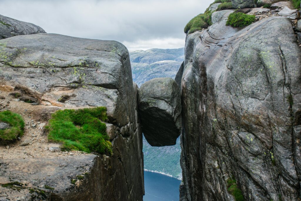 Kjeragbolten boulder wedged between steep cliffs above Lysefjord in Norway, showcasing a dramatic hiking viewpoint with rugged rock formations and distant fjord below.