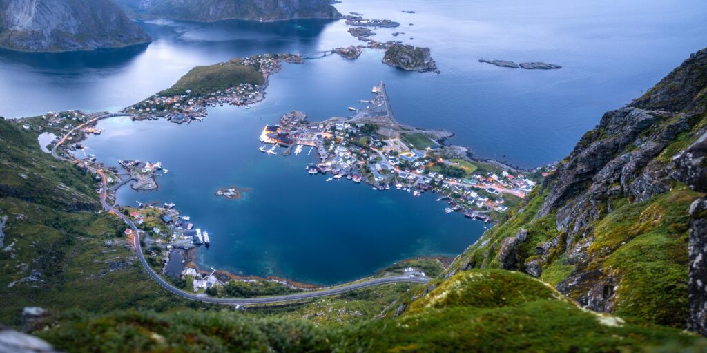 Panoramic view from Reinebringen in Norway overlooking Reine village, turquoise fjords, small islands, and dramatic coastal mountains in the Lofoten Islands.