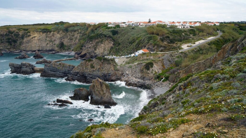scenic coastal cliffs along rota vicentina trail in portugal with ocean waves, rugged rocks, and hillside village - kayde parker
