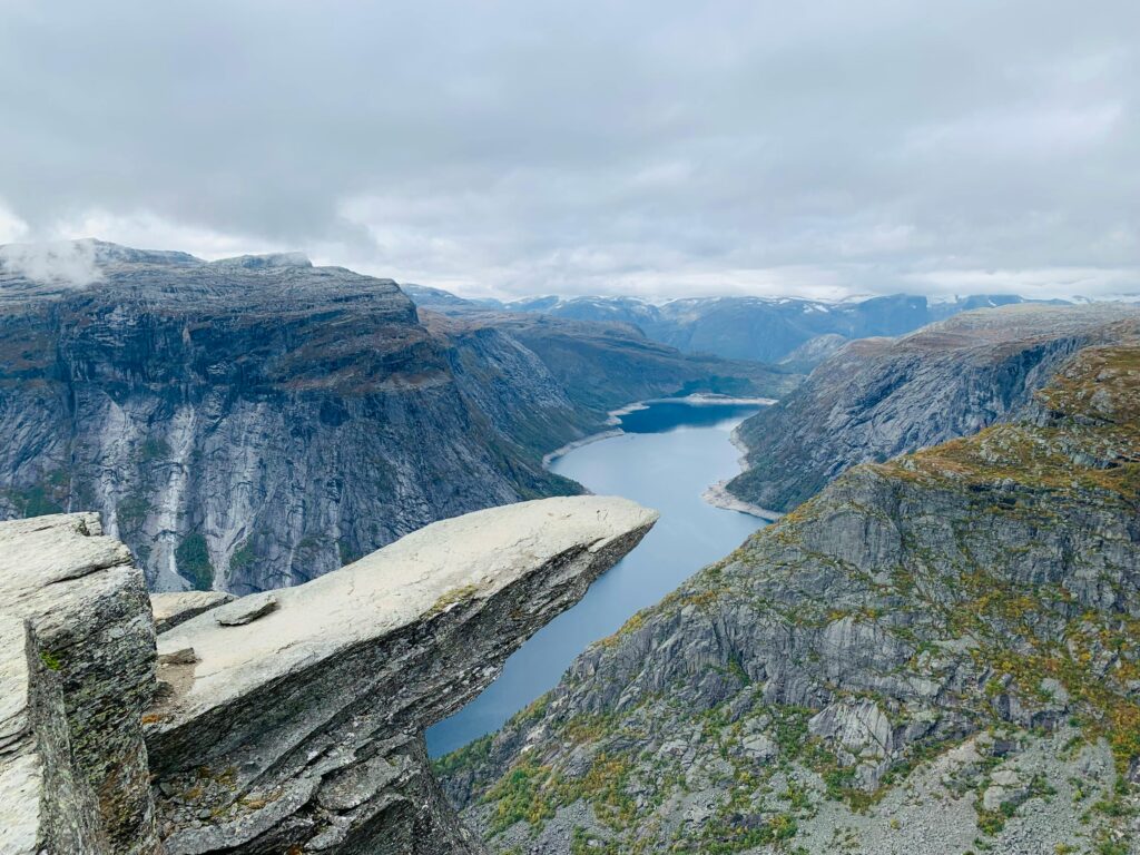 Trolltunga rock formation jutting out over a deep fjord in Norway, surrounded by rugged mountains and dramatic cloudy skies, captured from a hiking viewpoint.