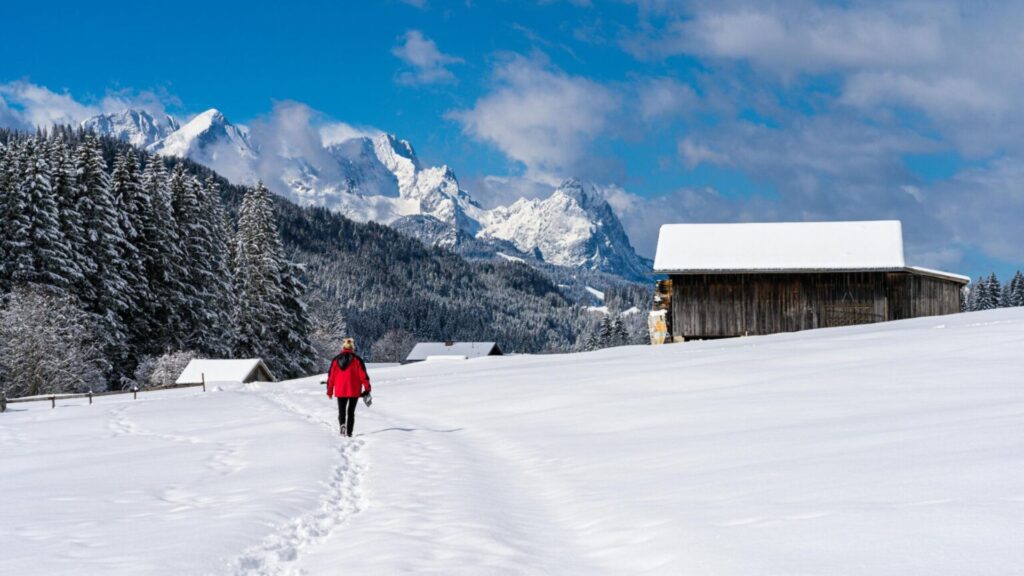 Winter walking holiday in Europe with person hiking through snowy mountains and alpine cabins