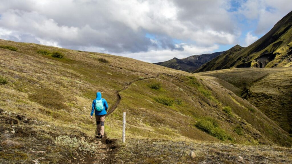 hiker walking along the laugavegur trail in iceland with dramatic mountains, rolling hills, and scenic landscapes in the highlands