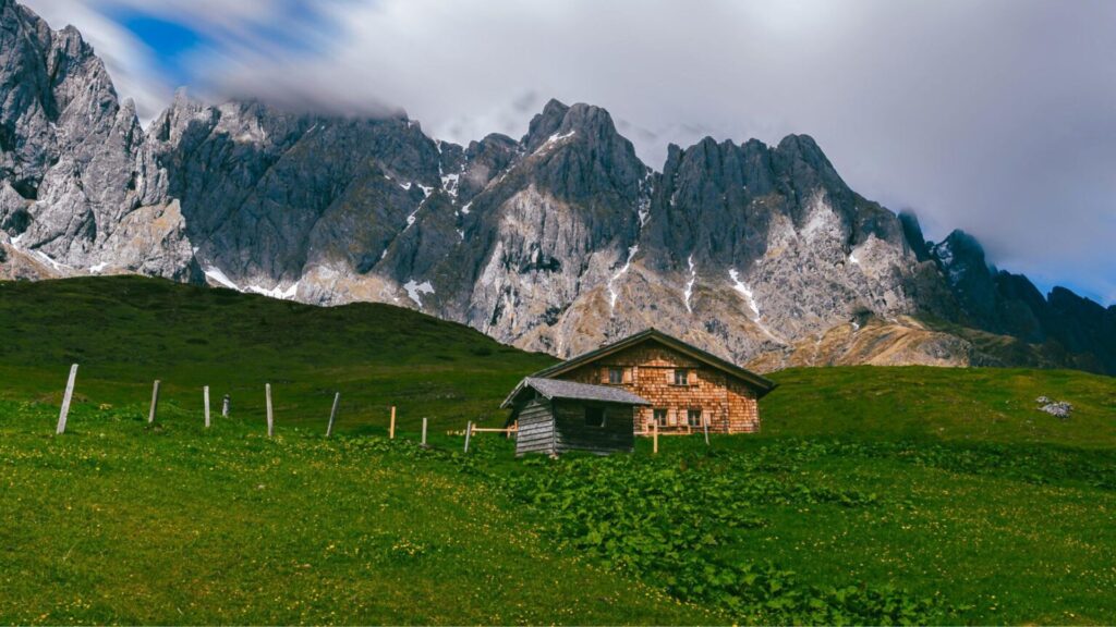 Scenic Austrian alpine hut surrounded by lush meadows and dramatic mountain peaks, ideal for hut-to-hut hiking in Austria.