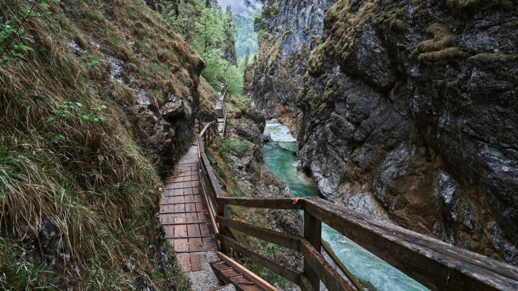 Leutasch Gorge trail in Austria with wooden walkway, steep rocky cliffs, and turquoise river flowing through a narrow alpine canyon
