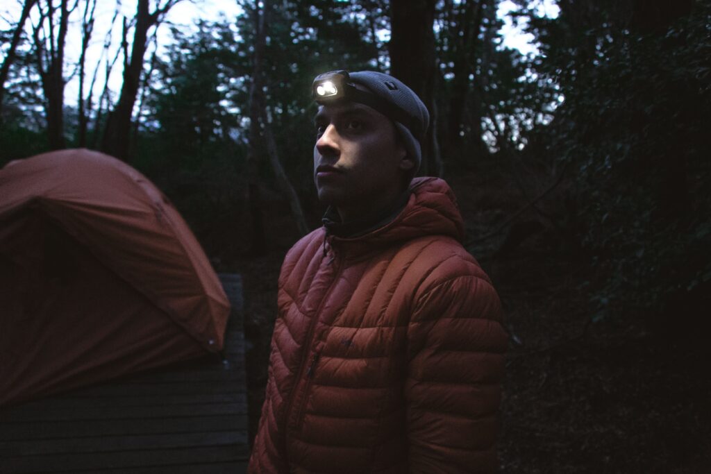 How a Headtorch Fits Into Your Overall Setup: camper wearing a headtorch beside a tent in a forest at dawn.