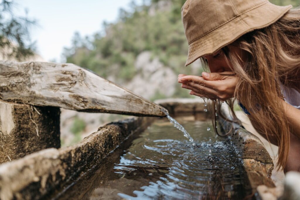 Hiker drinking from a mountain water source, highlighting hydration reservoirs for staying hydrated on the trail.