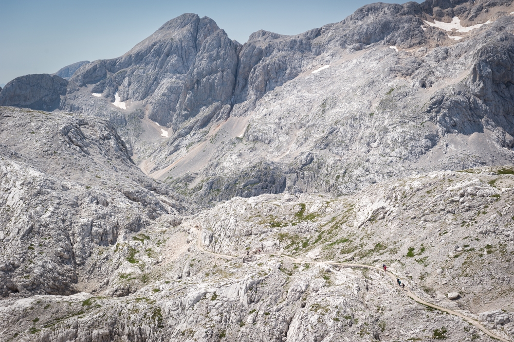 Hikers traverse rocky alpine terrain on the Juliana Trail, Slovenia, surrounded by dramatic mountain landscapes.