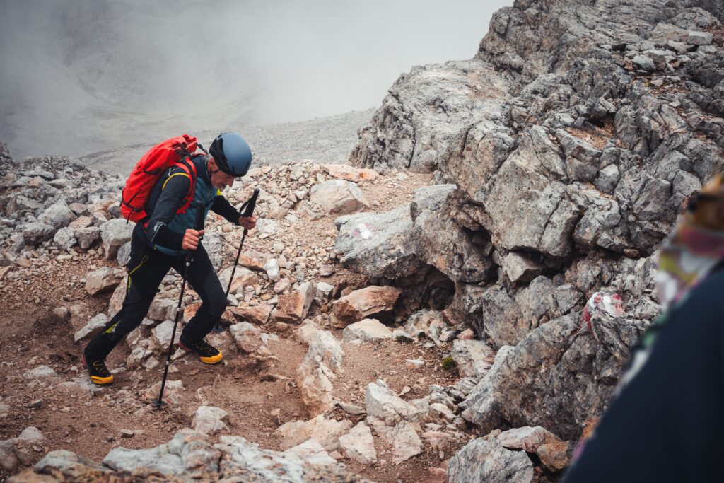 Hiker using trekking poles on rocky mountain trail, Uneven or Technical Terrain for better balance and stability.