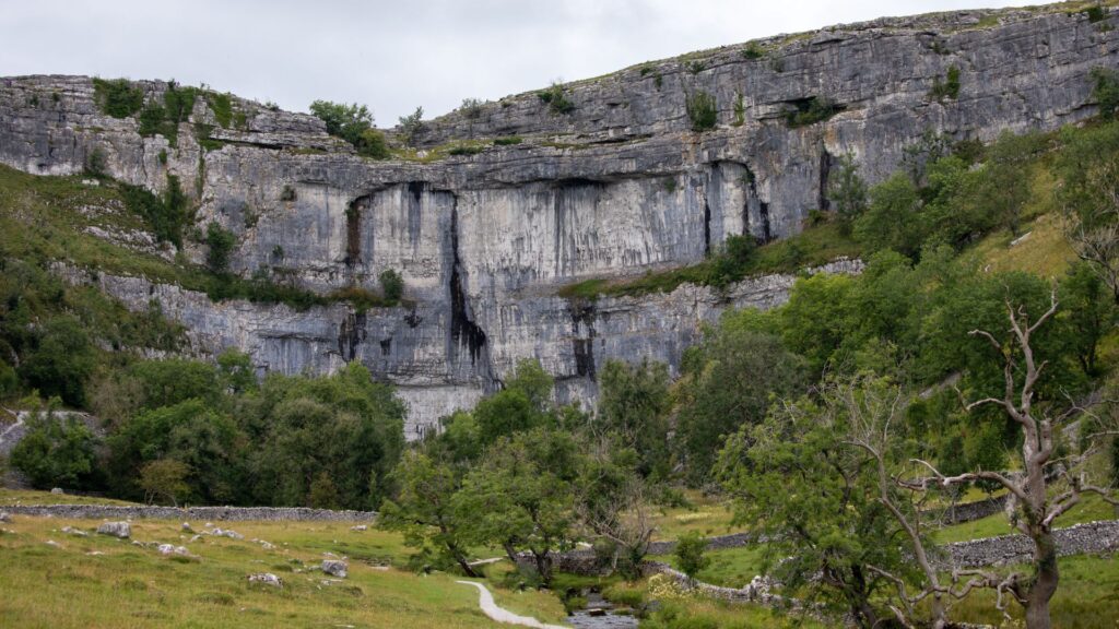 Limestone cliffs and valley on one of the best circular walks in Yorkshire near Malham Cove under cloudy skies.