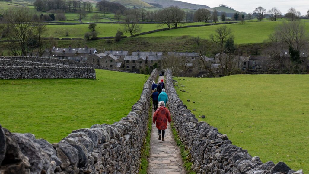 Best Walks in Yorkshire along a stone walled path leading to a picturesque village surrounded by rolling green countryside