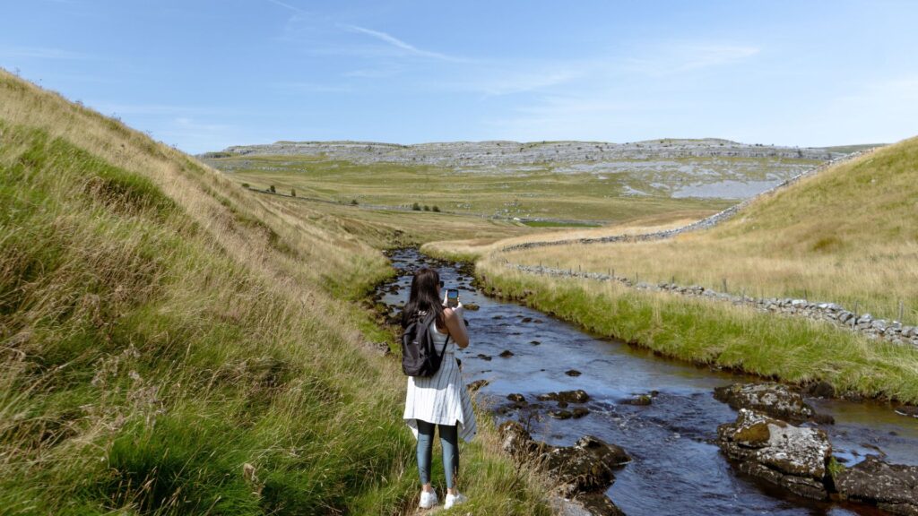 Person standing beside a stream in Yorkshire surrounded by rolling hills on a scenic countryside hiking adventure