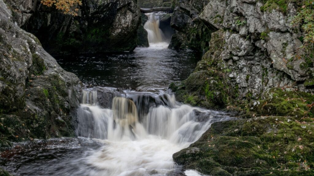 Scenic cascades and rocky gorge along the Ingleton Waterfall Trails in Yorkshire surrounded by moss covered cliffs