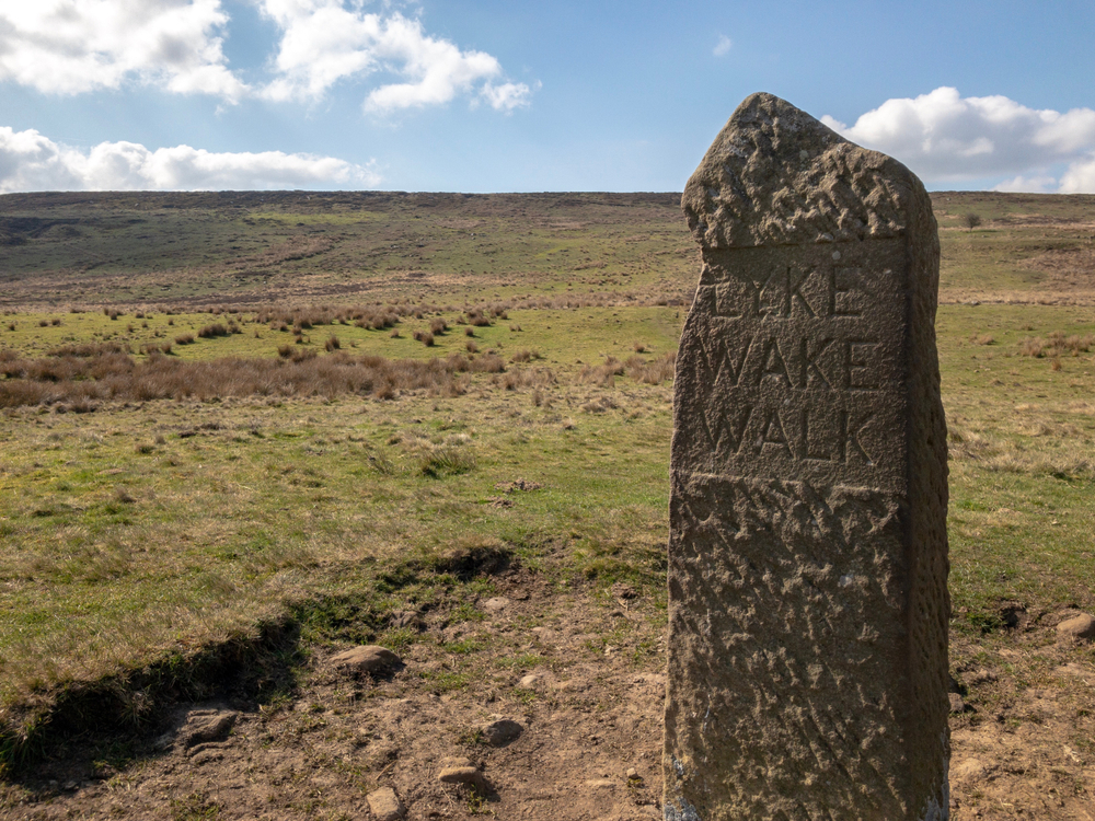 LykeWakeWalkMilestoneCodBeckReservoirNorthYorkshire Historic Lyke Wake Walk marker surrounded by open heather moorland in the North York Moors.