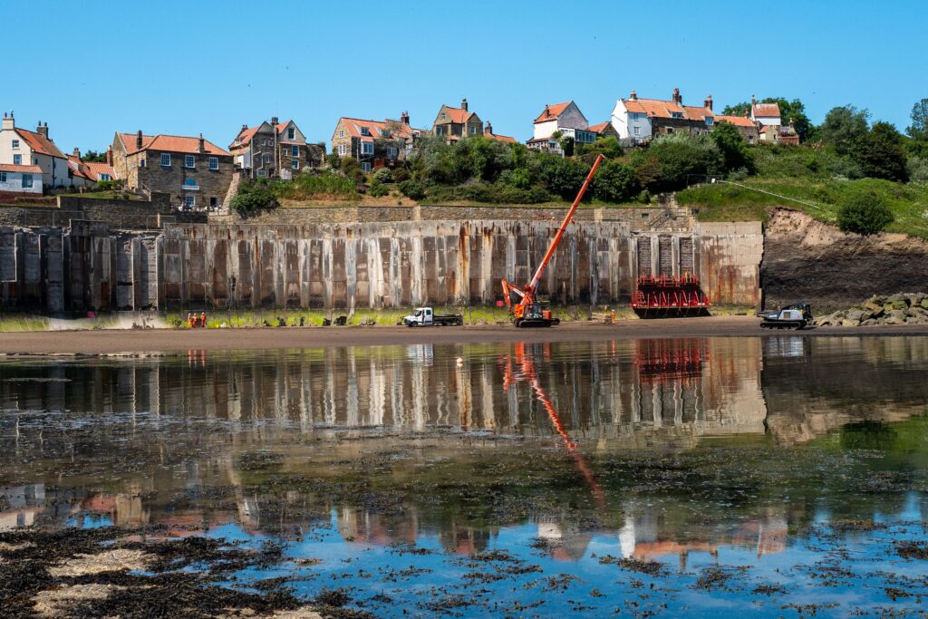 View of Robin Hoods Bay harbour and historic cottages reflected in calm water on the Yorkshire coast.