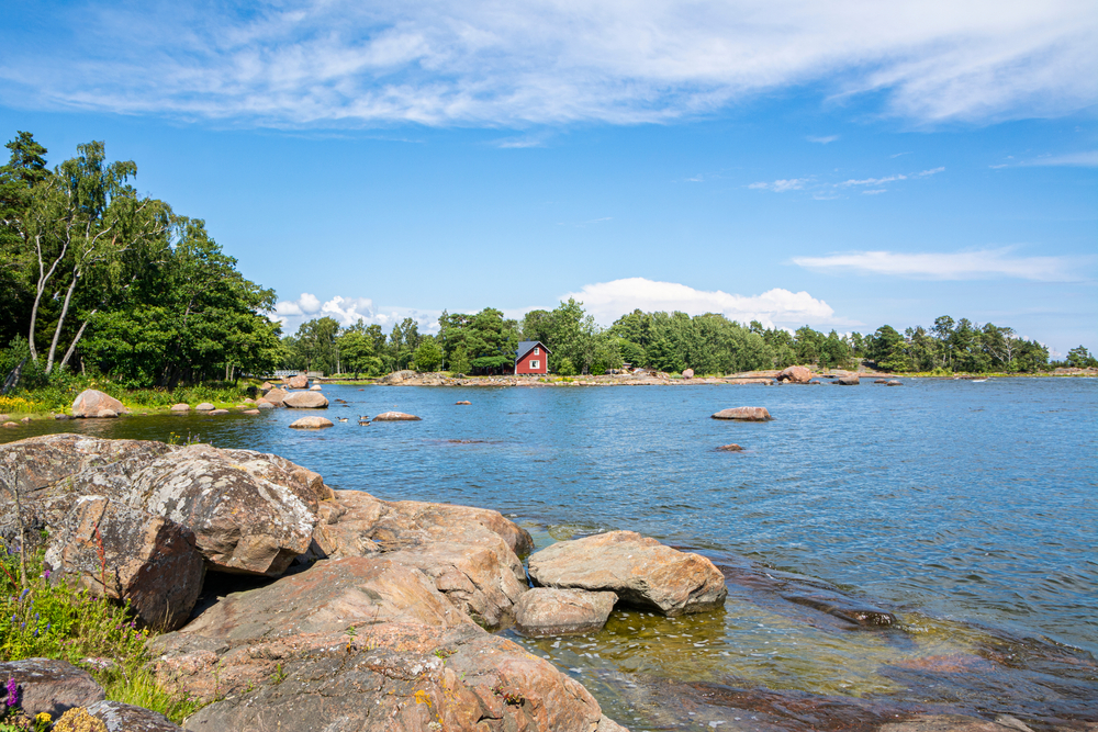CoastalViewOfPihlajasaariIslandAndGulfOfFinlandHelsinki Kayde Parker Pihlajasaari Island Circuit rocky coastal trail with blue sea green trees and a red island cottage