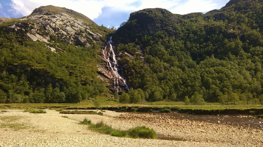 Steall Falls and the Nevis Gorge surrounded by lush forest rocky mountains and a scenic river in Scotland