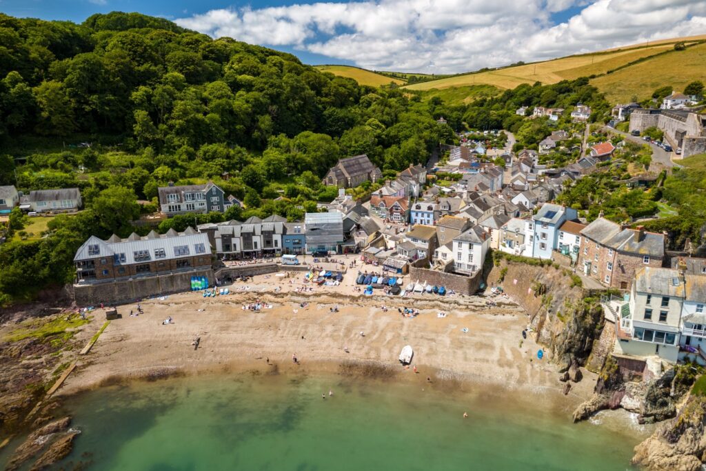 AerialViewOfACoastalVillageWithASandyBeach Kayde Parker Cornish coastal town with sandy beach colourful waterfront houses and green hills
