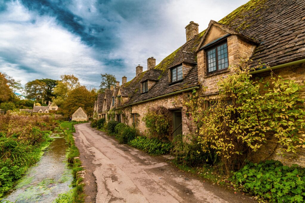 Bibury walk through charming Cotswold village with historic stone cottages mossy roofs and riverside scenery